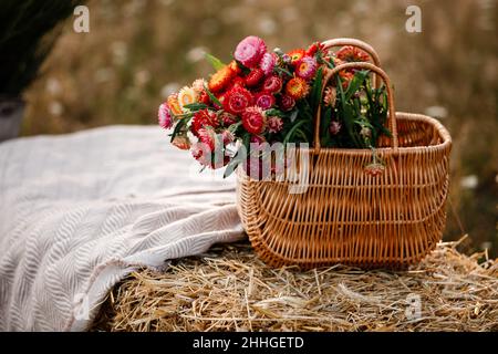 Strohkorb mit Blumen auf einem Strohstapel mit einer Leinentischdecke im Freien am sommersuny Tag bedeckt. Stockfoto