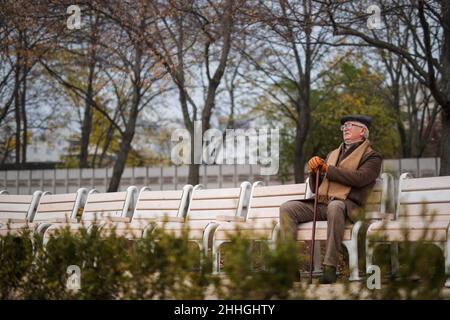 Ein alter eleganter Mann mit Spazierstock sitzt am Herbsttag auf der Bank im Park Stockfoto