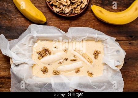 Ungekochte Teig Bananenbrot in der Form. Kochen. Holzhintergrund. Blick von oben. Süßes, vegetarisches Essen. Stockfoto