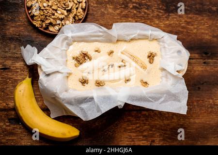 Ungekochte Teig Bananenbrot in der Form. Kochen. Holzhintergrund. Blick von oben. Süßes, vegetarisches Essen. Stockfoto