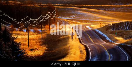 Alte Landstraße mit Drehungen und Kurven Telefon kabel in goldenes Sonnenlicht leuchtenden Stockfoto