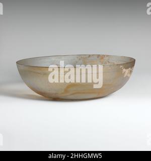 Glasschale Ende des 1st. Jahrhunderts v. Chr.–Anfang des 1st. Jahrhunderts n. Chr. römisch farblos mit hellgelbgrüner Färbung.abgerundeter vertikaler Rand; Seiten zu leicht unebenem, flachem Boden eingewellt.Dekoration von horizontalen Radnuten im Innenraum, bestehend aus einer einzigen breiten Nut unter dem Rand und einem Band aus zwei schmalen Nuten um den Unterkörper.intakt; Viele Nadelstichtblasen; Abstumpfen, Lochfraß und Verwitterung, Und brillante Irideszenz, mit einigen Flecken der ursprünglichen polierten Oberfläche. Farblose flache Glasschale mit eingeschnittenen Linien. Glasschale. Römisch. Spätes 1st Jahrhundert B.C.–frühes 1st Jahrhundert A.D.. Glas; gegossen und geschnitten. Stockfoto