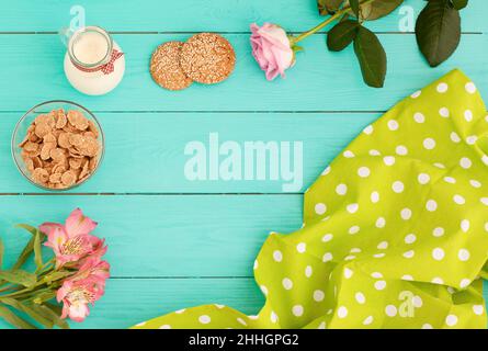 Rahmen von Morgenmahlgut mit Krug Milch, Keksen und Haferflocken auf blauem Holzhintergrund. Tischdecke in Tupfen und Blumen. Draufsicht. Modell. Cop Stockfoto