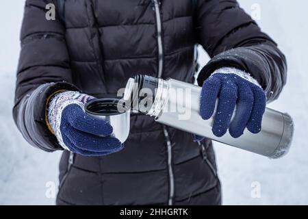 Im Winter gießt eine Frau auf Gewicht Tee aus einer Thermoskanne in ein Glas. Hochwertige Fotos Stockfoto