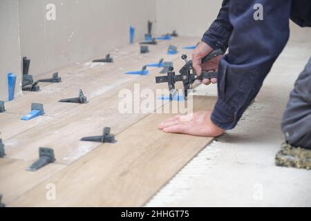 Mason Hände Anpassung Fliesenwader zwischen Keramik-Holz-Effekt Fliesen. Stockfoto