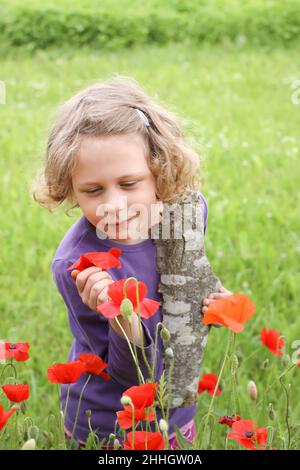 Nettes kleines Mädchen, das im Sommer auf dem Land auf einer Wiese mit blühenden roten Mohnblumen spielt. Stockfoto