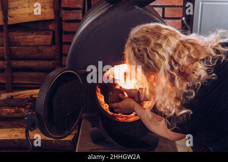 Frau heizt den bullerjan-Ofen. Home Holzofen Brennofen Heizgerät im Haus Innenraum, mit Stapel von Brennholz daneben. Stockfoto