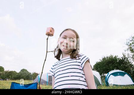 Porträt eines lächelnden Mädchens mit Marschmalow auf dem Stock auf dem Campingplatz Stockfoto