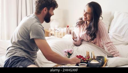 Jeder Morgen ist etwas Besonderes für Sie. Aufnahme eines glücklichen jungen Paares, das zu Hause im Bett zusammen frühstücken kann. Stockfoto