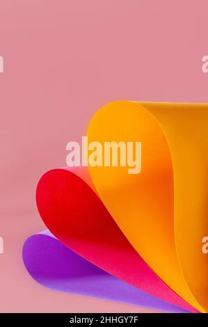 Buntes Papier in Gelb, Rot und Violett wirbelt auf korallenrosa Hintergrund Stockfoto