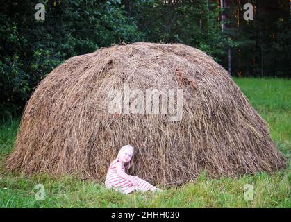 Kleines Mädchen in der Nähe eines Heuschocks auf einem Feld auf dem Land im Sommer. Stockfoto