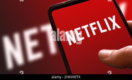 Netflix rotes Logo auf Handy-Display mit Rampenfarbe im Hintergrund. Streaming-Filme und TV-Serie Plattform-Symbol auf Smartphone-Bildschirm halten Stockfoto
