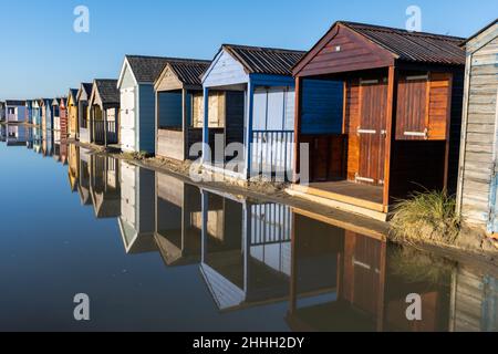 Eine Reihe von bunten Strandhütten spiegelt sich in einer großen Pfütze am West Wittering Beach, Chichester, Großbritannien, wider Stockfoto