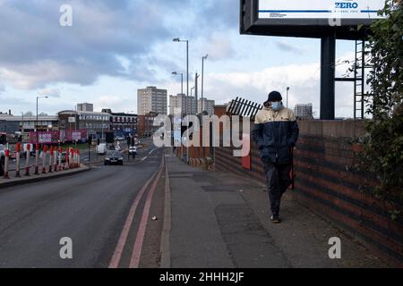 Mann mit Gesichtsmaske entlang der A34 in Richtung Wohngebäude in Lozells und East Handsworth von Newtown in der Nähe des Stadtzentrums am 5th. Januar 2022 in Birmingham, Großbritannien. Lozells ist ein ethnisch vielfältiges innerstädtische Gebiet in West Birmingham, England, und ist Teil der Stadtteile von Lozells und East Handsworth und liegt zwischen den Stadtteilen Handsworth und Aston. Die Wohnungen in Lozells bestehen hauptsächlich aus Reihenhäusern, die gebaut wurden, als das Gebiet industrialisiert wurde und die Arbeiter Wohnraum benötigten. Das Gehäuse ist eine Mischung aus privaten und ratswohnungen, mit einigen neueren Post Stockfoto