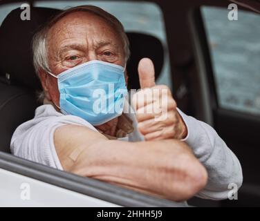 Das war nicht so schlimm. Aufnahme eines älteren Mannes, der bei einer Fahrt durch die Impfstelle einen Daumen nach oben in seinem Auto zeigte. Stockfoto