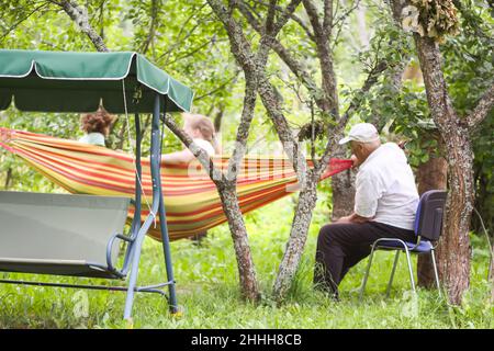 Großeltern schieben ihre Enkelinnen in eine Hängematte im Garten. Stockfoto