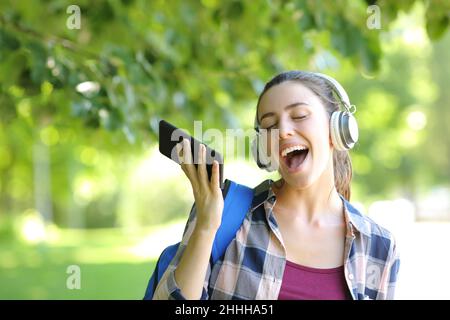 Fröhlicher Student, der Kopfhörer trägt und Smartphone hält, um in einem Park Musik zu hören und zu singen Stockfoto