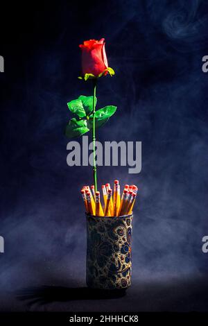 Dieses Foto, das mit wirklichem Rauch, einer roten Rose und ein paar Bleistiften erstellt wurde, verleiht dem Bild ein mystisches Aussehen, ideal für ein Poster Stockfoto