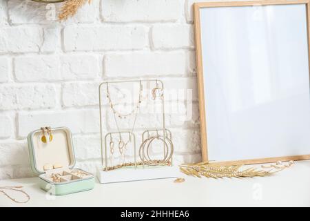 Stilvoller Schmuck und leerer Bilderrahmen auf dem Tisch in der Nähe der weißen Ziegelwand Stockfoto