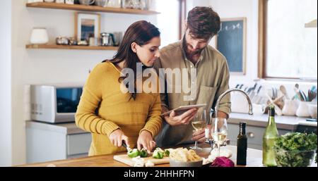 Teamarbeit macht das Rezept zum Erfolg. Aufnahme eines jungen Paares, das ein digitales Tablet verwendet, während es zu Hause eine Mahlzeit zubereitet. Stockfoto
