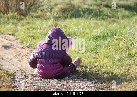 Ein kleines Mädchen im purpurnen Parka, das im Frühlingspark spielt Stockfoto