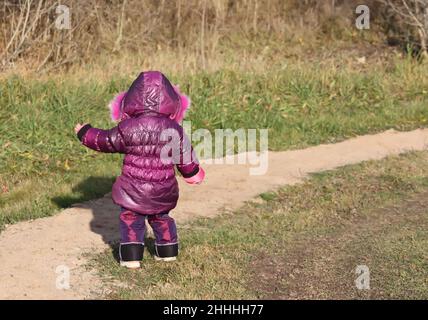 Ein kleines Mädchen im purpurnen Parka, das im Frühlingspark spielt Stockfoto