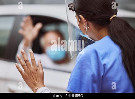 Bis bald. Aufnahme eines nicht erkennbaren Arztes, der auf einer Fahrt durch die Impfstelle einen Patienten anwinkt. Stockfoto