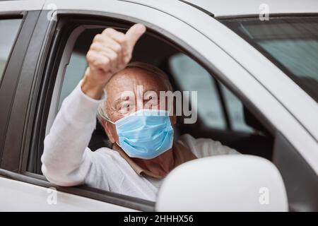 Daumen hoch für die Impfung. Aufnahme eines älteren Mannes, der bei einer Fahrt durch die Impfstelle einen Daumen nach oben in seinem Auto zeigte. Stockfoto