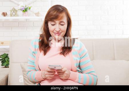 Brünette Frau mittleren Alters, modisches Model, trägt moderne Kleidung und schreibt mit ihrem Smartphone im Hintergrund. Hausfrau. Speicherplatz nachahmen und kopieren Stockfoto