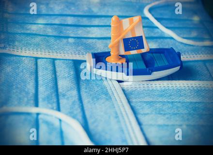 Boot mit der Flagge Europas, das inmitten von chirurgischen Masken segelt. Stockfoto