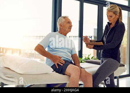 Die Behandlung beginnt mit einer genauen Diagnose. Aufnahme eines älteren Mannes, der sich in ihrem Büro mit seinem Physiotherapeuten beraten hat. Stockfoto