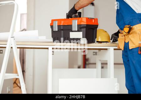 Ausgeschnittene Aufnahme von Bauunternehmern in Overalls, die Werkzeugkasten auf den Tisch legen, bereit für Bauarbeiten Stockfoto