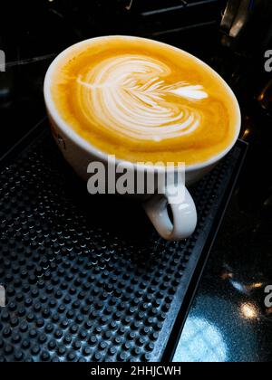 Rosette mit Herz-Latte-Kunst in einer großen Tasse, die auf einer schwarzen Gummimatte steht Stockfoto