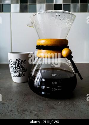 Eine chemex-ähnliche Tasse mit schwarz gefiltertem Kaffee mit weißer Tasse mit Kalligrafie-Schriften für Kaffee Stockfoto