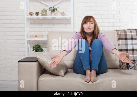 Im mittleren Alter schöne Brünette Frau verwirrt zu Hause Hintergrund. Wechseljahre Stockfoto