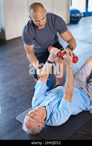 Ihn zurück zum Wohlbefinden führen. Aufnahme eines Physiotherapeuten, der einem älteren Mann mit Gewichten hilft. Stockfoto