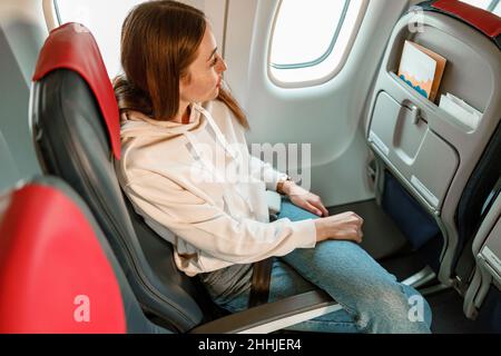 Junge Frau, die im Flugzeug auf dem Passagierstuhl sitzt Stockfoto