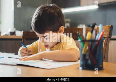 Kaukasischer kleiner Junge, der Alphabet lernt. Junge schreibt Hausaufgaben. Quarantäne-Lebensstil. Stockfoto