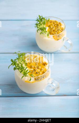 Mangojoghurt mit Passionsfrucht und Koriander-Microgreen im Glas auf blauem Holzhintergrund. Seitenansicht, Nahaufnahme. Stockfoto