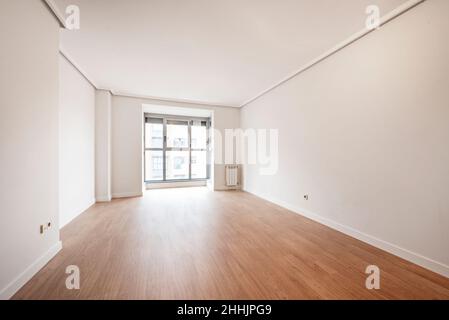 Leeres Wohnzimmer mit großem Fenster im Hintergrund, Holzböden und weiß gestrichenen Wänden Stockfoto