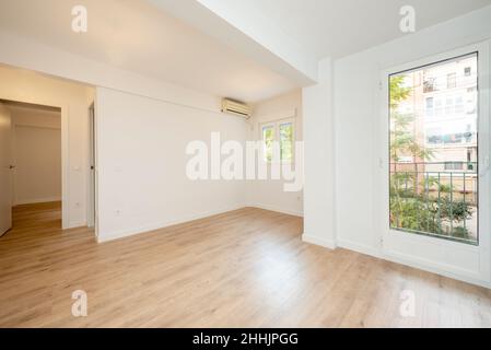 Leeres Wohnzimmer mit großem Fenster zur einen Seite, Eichenholzböden, Klimaanlage und weiß gestrichenen Wänden Stockfoto