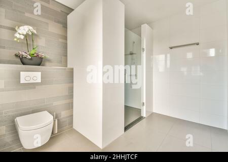 Duschkabine aus Glas und eine weiße Toilettenschüssel im Badezimmer mit gefliesten Wänden, die mit blühenden Orchideenblüten dekoriert sind Stockfoto