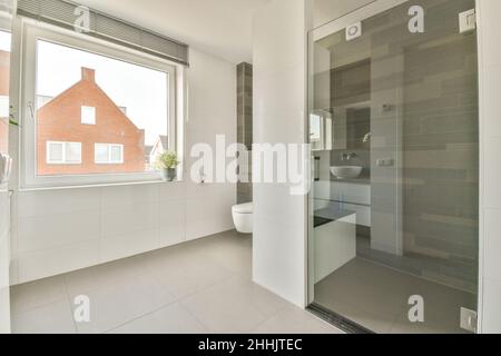 Duschkabine aus Glas und eine weiße Toilettenschüssel im Badezimmer mit gefliesten Wänden, die mit blühenden Orchideenblüten dekoriert sind Stockfoto