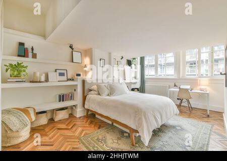 Interieur des modernen, stilvollen Schlafzimmers mit komfortablem Bett mit weißen Kissen und Decken-Regalen und Parkettboden Stockfoto