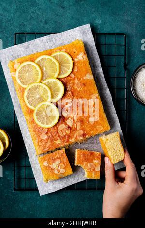 Draufsicht auf Ernte anonyme Person, die quadratische Scheibe von leckeren hausgemachten Zitronenkuchen auf Metallgestell in der Küche platziert Stockfoto