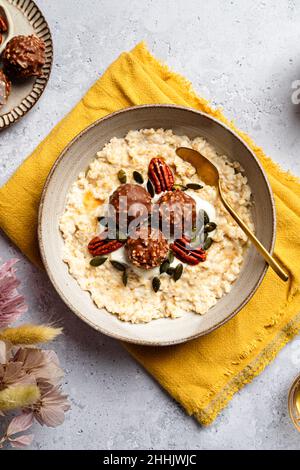 Hohe Winkel der Schüssel mit leckeren Milch Haferflocken serviert mit knusprigen Schokoladenkugeln Kürbiskerne und Pekannuss auf Serviette für ein gesundes Frühstück Stockfoto