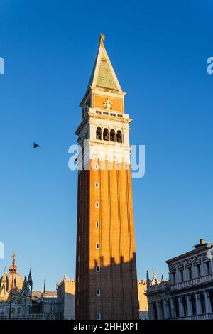 Von unten der Fassade des hohen Glockenturms der alten Markusbasilika mit ornamentalen Details auf dem Platz in Venedig unter klarem blauen Himmel Stockfoto