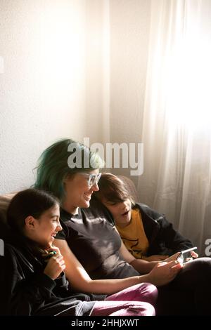 Mutter mit zufriedenen ethnischen Kindern, die Interessantes Video auf dem Handy anschauen, während sie zusammen auf der Couch im Wohnzimmer zu Hause sitzt Stockfoto