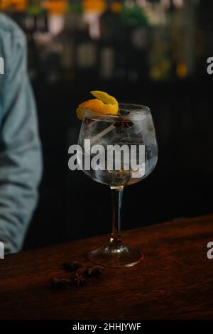 Crop unkenntlich Barkeeper serviert Weinglas mit Gin und Tonic Cocktail dekoriert mit Orangenschale auf Holztheke in der Bar Stockfoto