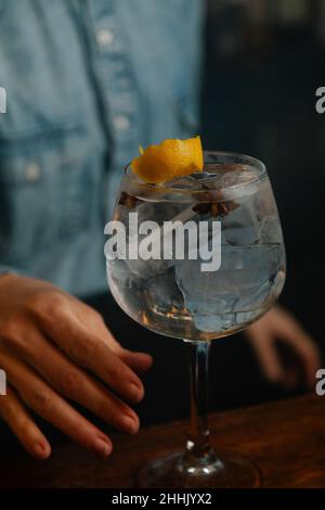 Weicher Fokus der zugeschnittenen, nicht erkennbaren Barkeeperin, die mit Zangen Zitronenschale in Glas mit Eiswürfeln setzt, während sie in der Bar einen Cocktail zubereitet Stockfoto